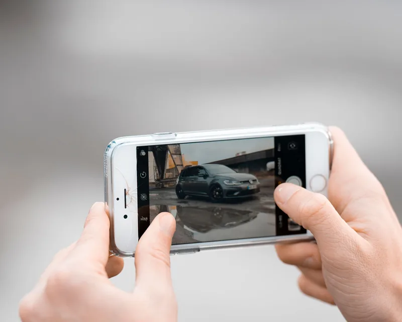 Kéz mobiltelefonnal fényképez egy autót, a kijelzőn látszik a kép